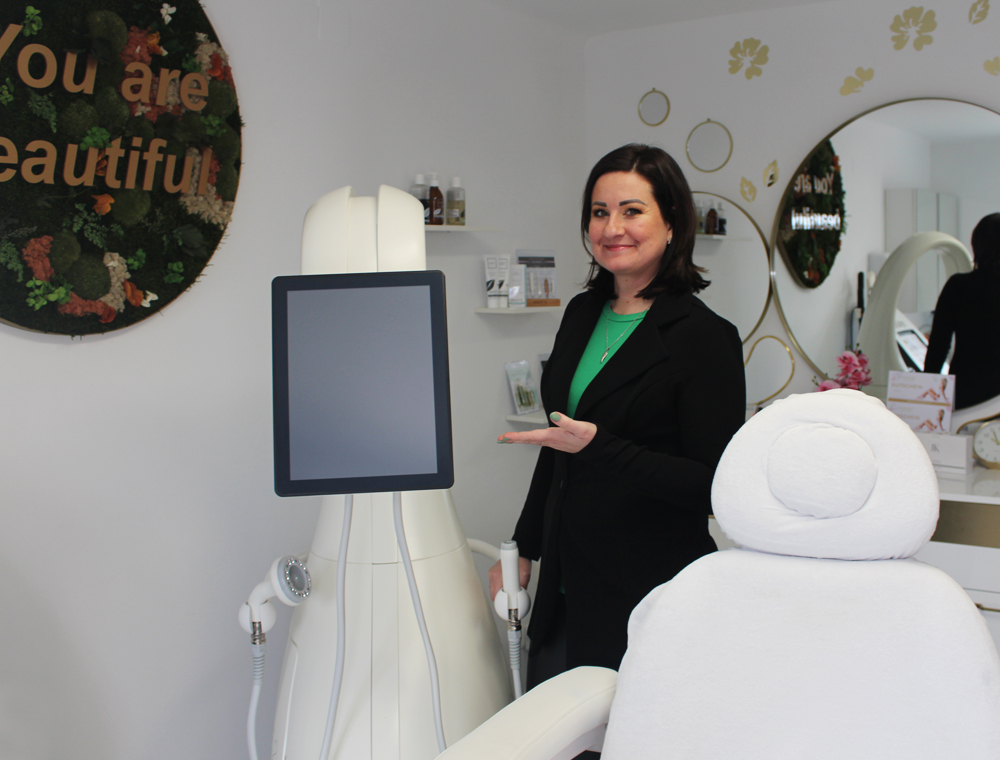 Foto von der Kosmetikerin Moni, im Schönheitssalon Noblesse, die mit einer einladenden Geste auf den effizienten T-Shape 2 zeigt